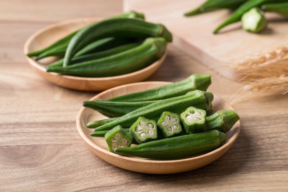 Gombo : 10 Secrets Révélés sur ce Légume Extraordinaire et Ses Bienfaits ! 2 Gombos frais verts coupés sur une planche à découper en bois