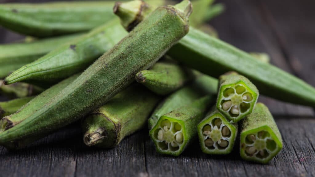 Gombo : 10 Secrets Révélés sur ce Légume Extraordinaire et Ses Bienfaits ! 3 Gombos frais verts coupés sur une planche à découper en bois