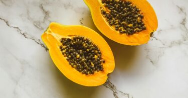 Graines de papaye fraîches noires et brillantes à côté d'une tranche de papaye orange vif.