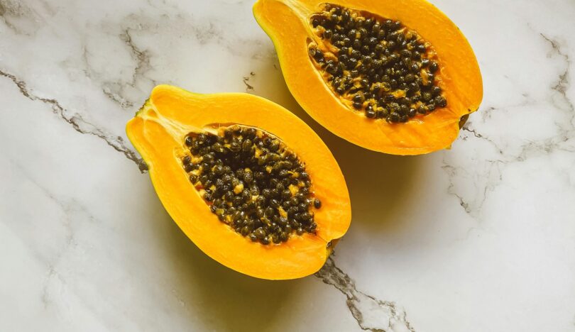 Graines de papaye fraîches noires et brillantes à côté d'une tranche de papaye orange vif.